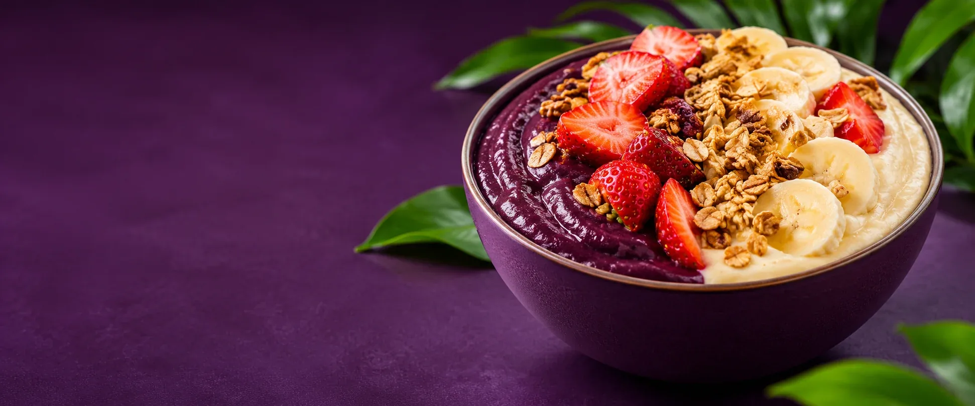 Tigela dividida entre açaí e creme, com morangos, banana e granola